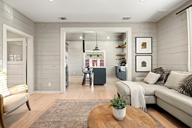 living area featuring wooden walls, baseboards, visible vents, and light wood finished floors