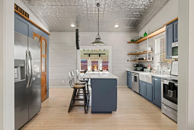 kitchen featuring light wood-style flooring, blue cabinetry, an ornate ceiling, and stainless steel appliances