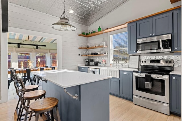 kitchen featuring a kitchen bar, an ornate ceiling, stainless steel appliances, wooden walls, and light countertops