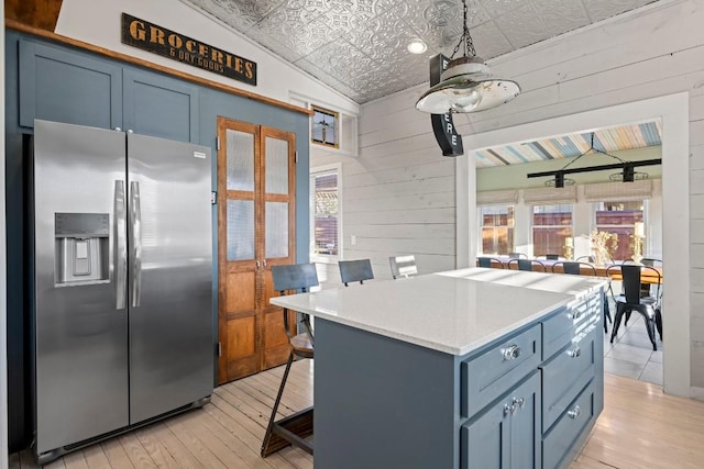 kitchen featuring wood walls, light wood-type flooring, stainless steel refrigerator with ice dispenser, plenty of natural light, and an ornate ceiling