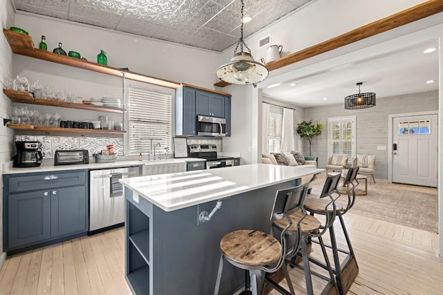 kitchen featuring a breakfast bar area, open shelves, blue cabinetry, light countertops, and appliances with stainless steel finishes