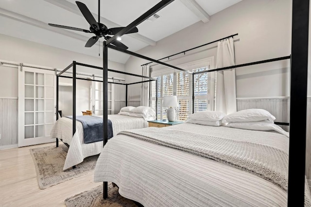 bedroom with wood finished floors, vaulted ceiling with beams, visible vents, and a wainscoted wall