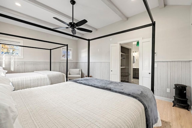 bedroom with beam ceiling, a wainscoted wall, light wood finished floors, and a ceiling fan