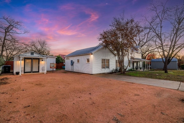 back of house at dusk featuring an outbuilding, metal roof, and fence