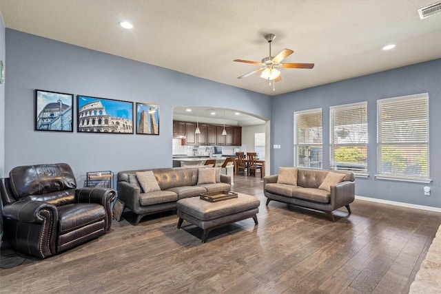 living room with visible vents, dark wood finished floors, arched walkways, baseboards, and ceiling fan