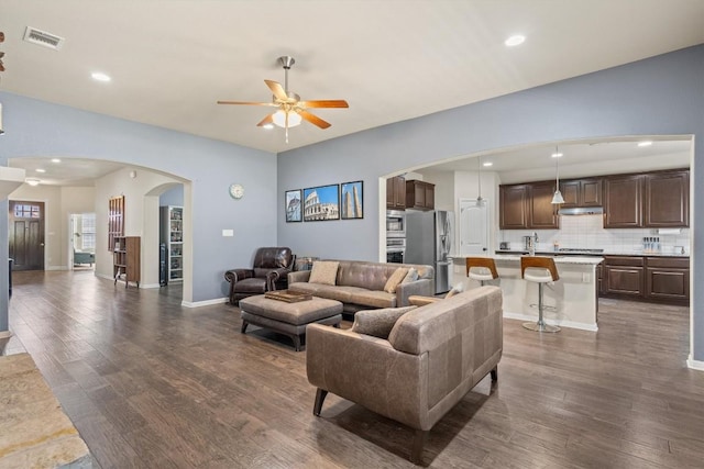 living room featuring arched walkways, visible vents, dark wood-type flooring, and a ceiling fan