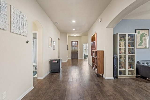 hallway with visible vents, wood finished floors, arched walkways, and baseboards