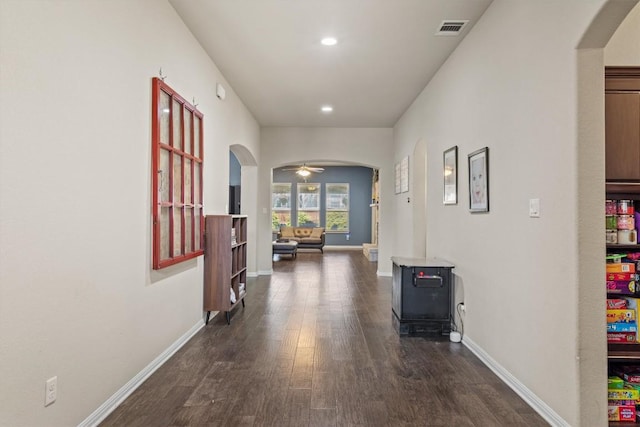 corridor with arched walkways, visible vents, dark wood finished floors, and baseboards