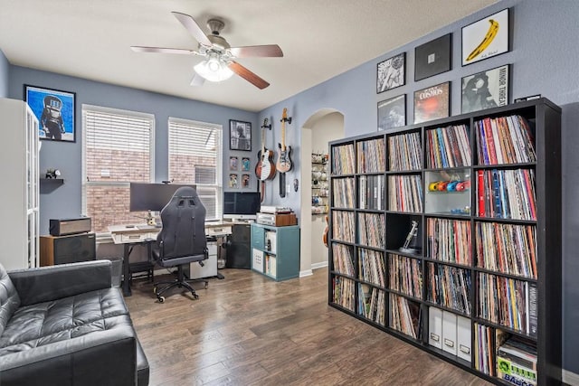 home office featuring arched walkways, ceiling fan, and wood finished floors