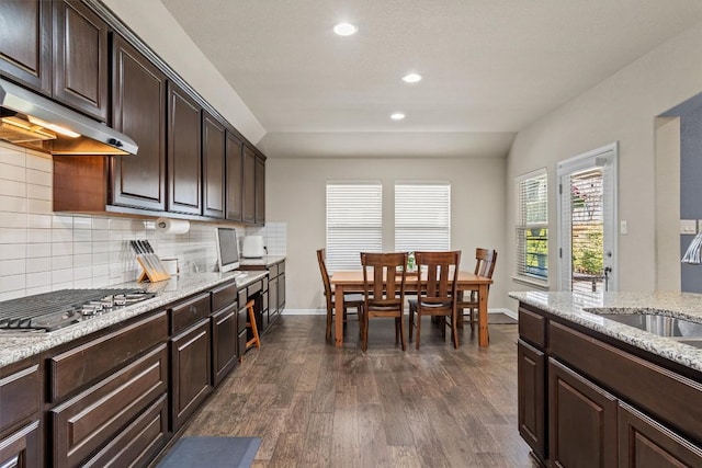 kitchen with dark wood-type flooring, under cabinet range hood, a sink, stainless steel gas stovetop, and decorative backsplash