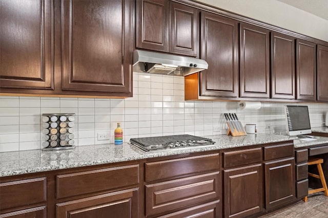 kitchen with dark brown cabinetry, stainless steel gas stovetop, backsplash, and under cabinet range hood