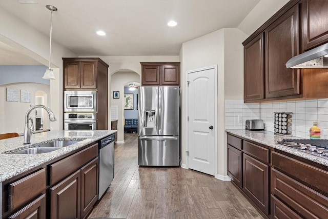 kitchen with dark wood-type flooring, a sink, tasteful backsplash, arched walkways, and appliances with stainless steel finishes