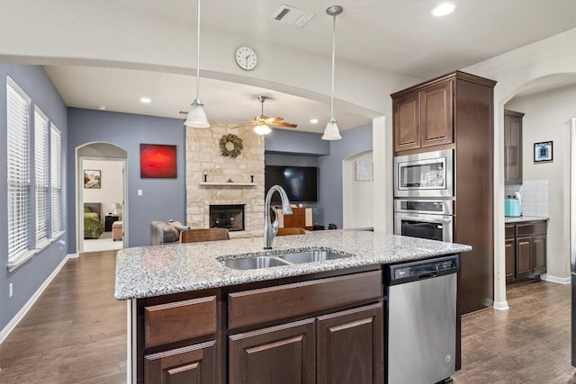 kitchen featuring visible vents, a sink, stainless steel appliances, a stone fireplace, and ceiling fan