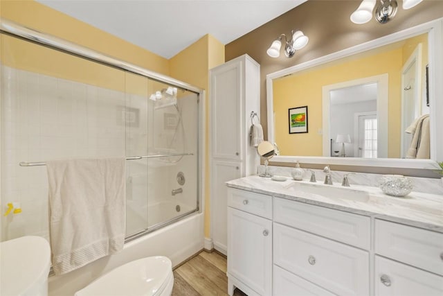 full bath with enclosed tub / shower combo, toilet, wood finished floors, and vanity