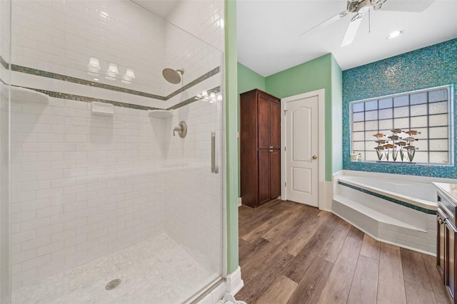 full bath featuring a ceiling fan, a garden tub, wood finished floors, and a shower stall