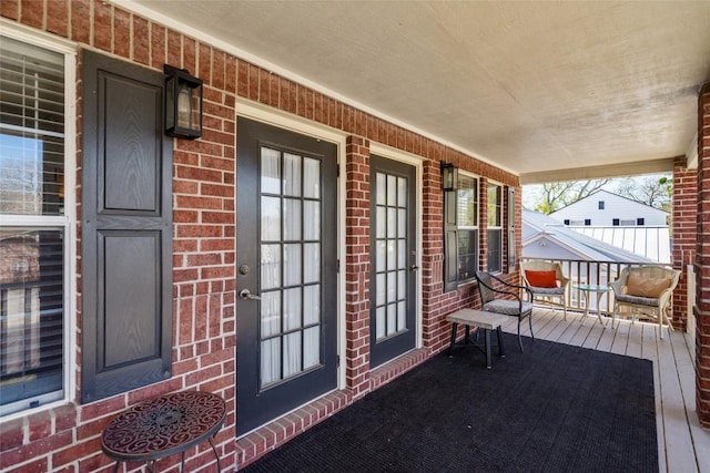 view of exterior entry featuring brick siding and covered porch