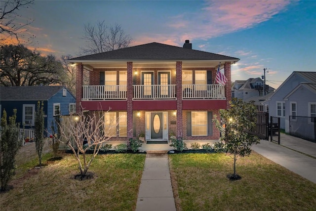 view of front facade with a front lawn, a balcony, fence, brick siding, and a chimney