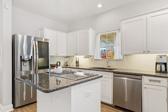 kitchen featuring dark stone counters, a sink, decorative backsplash, stainless steel appliances, and white cabinetry