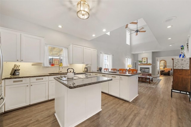 kitchen featuring wood finished floors, a ceiling fan, a peninsula, a sink, and white cabinets