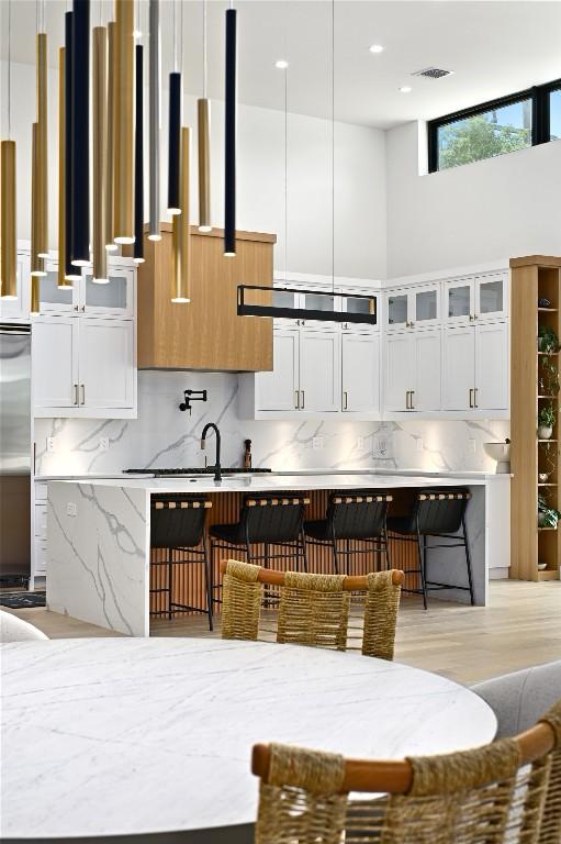 kitchen featuring visible vents, glass insert cabinets, tasteful backsplash, and white cabinetry