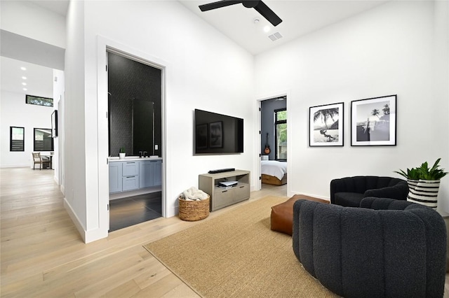 living area with visible vents, baseboards, light wood-style flooring, high vaulted ceiling, and a ceiling fan