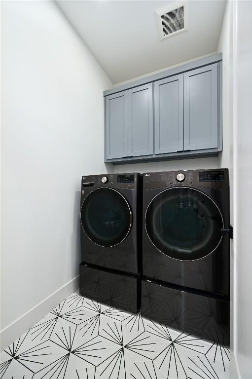 laundry area featuring washing machine and clothes dryer, visible vents, tile patterned flooring, baseboards, and cabinet space