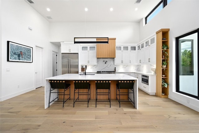 kitchen featuring stainless steel built in refrigerator, tasteful backsplash, a high ceiling, white cabinets, and light wood finished floors