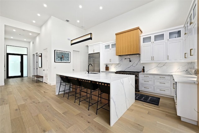 kitchen featuring light wood-style flooring, high quality appliances, a towering ceiling, and a sink