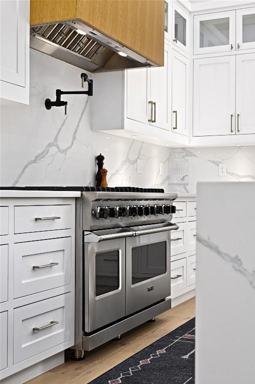 kitchen with double oven range, glass insert cabinets, wall chimney exhaust hood, white cabinets, and decorative backsplash