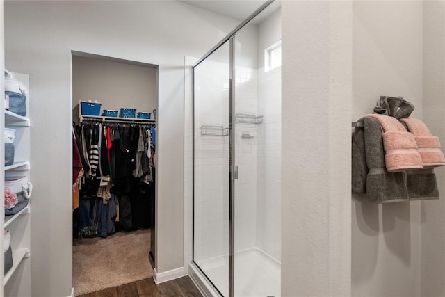 bathroom featuring a shower stall, a walk in closet, and wood finished floors