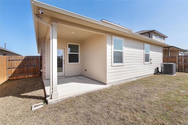 rear view of property with a patio area, central air condition unit, a lawn, and a fenced backyard