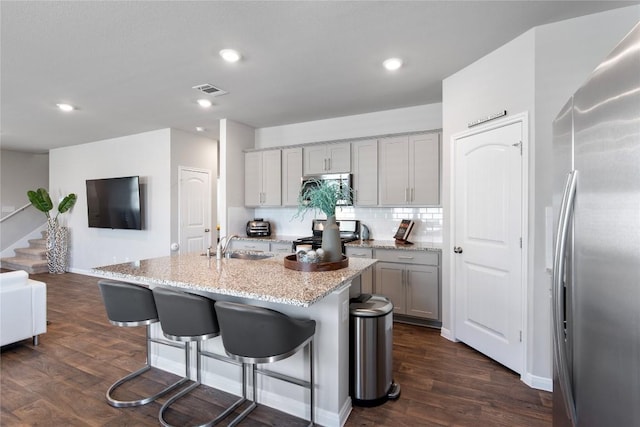 kitchen featuring visible vents, dark wood finished floors, a breakfast bar, stainless steel appliances, and decorative backsplash