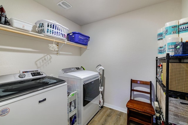 clothes washing area featuring visible vents, baseboards, laundry area, wood finished floors, and independent washer and dryer