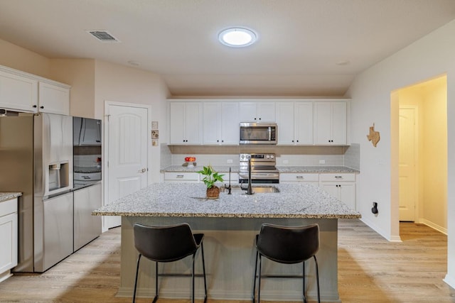 kitchen with light wood-type flooring, visible vents, a kitchen breakfast bar, white cabinetry, and stainless steel appliances