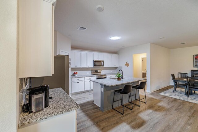 106 Pelican Ct, Bastrop, TX 78602 - kitchen featuring stainless steel appliances, light wood-type flooring, white cabinets, and a breakfast bar area