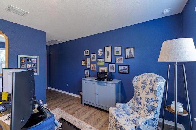 office space with a textured ceiling, wood finished floors, visible vents, and baseboards