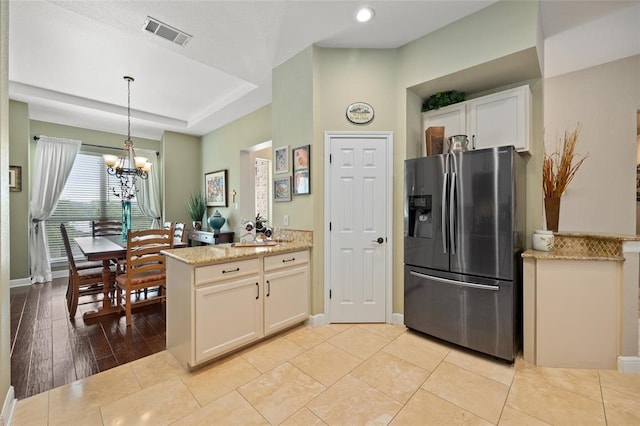 kitchen with visible vents, light stone countertops, a peninsula, an inviting chandelier, and stainless steel fridge