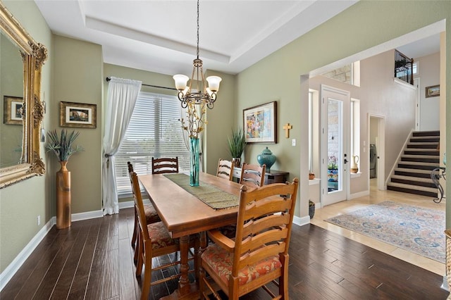 dining room with an inviting chandelier, a raised ceiling, dark wood-style floors, and baseboards