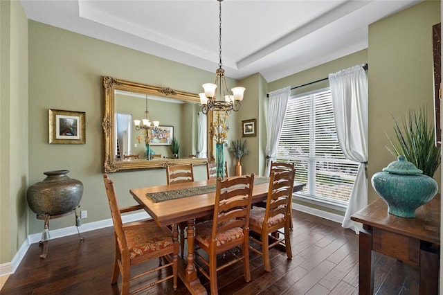 dining area with a tray ceiling, hardwood / wood-style flooring, a notable chandelier, and baseboards