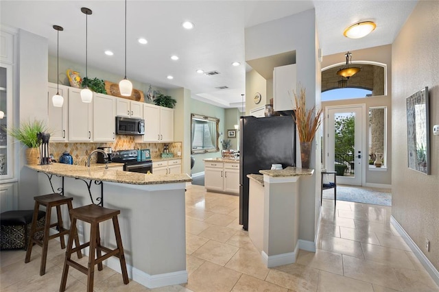 kitchen with light stone counters, tasteful backsplash, white cabinetry, appliances with stainless steel finishes, and a peninsula