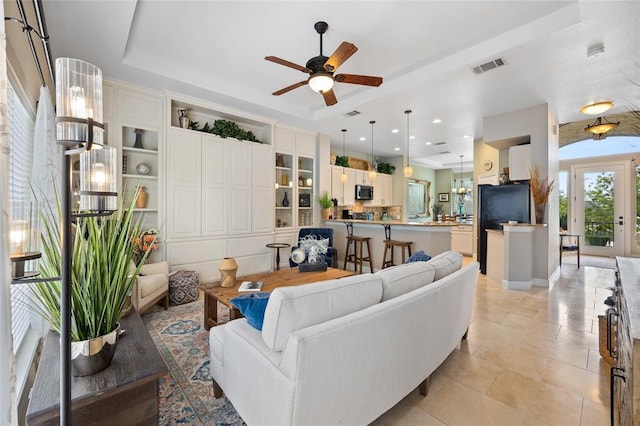 living area with a tray ceiling, light tile patterned floors, visible vents, and ceiling fan