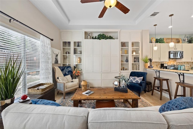 living area with visible vents, a raised ceiling, and a ceiling fan