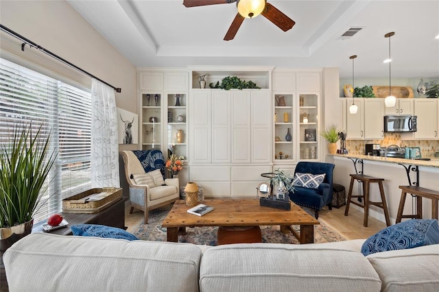 living room with ceiling fan, a tray ceiling, visible vents, and plenty of natural light