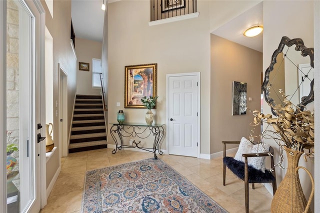 entryway with stairway, light tile patterned flooring, baseboards, and a towering ceiling