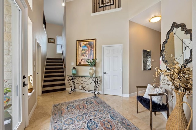 entryway featuring stairway, light tile patterned floors, a high ceiling, and baseboards