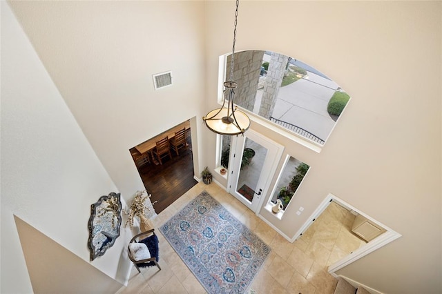 living room with tile patterned floors, visible vents, baseboards, and a towering ceiling