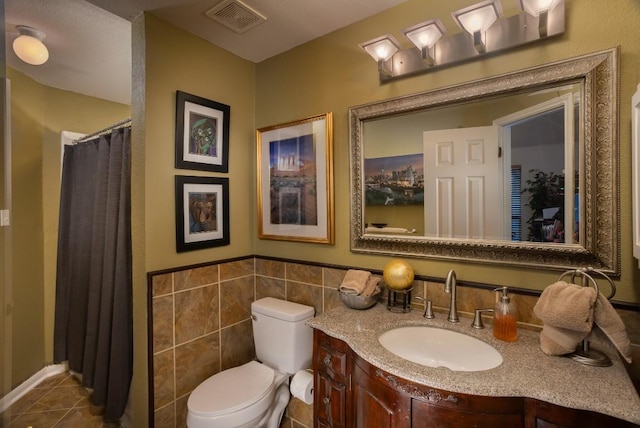 bathroom featuring tile patterned flooring, visible vents, tile walls, toilet, and vanity