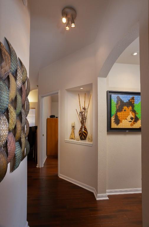 hallway featuring baseboards, arched walkways, and wood finished floors