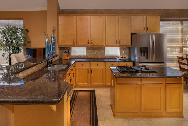 kitchen with a sink, gas stovetop, dark stone counters, a peninsula, and stainless steel fridge with ice dispenser