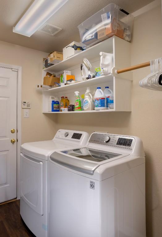 clothes washing area featuring washer and dryer, laundry area, visible vents, and dark wood-type flooring